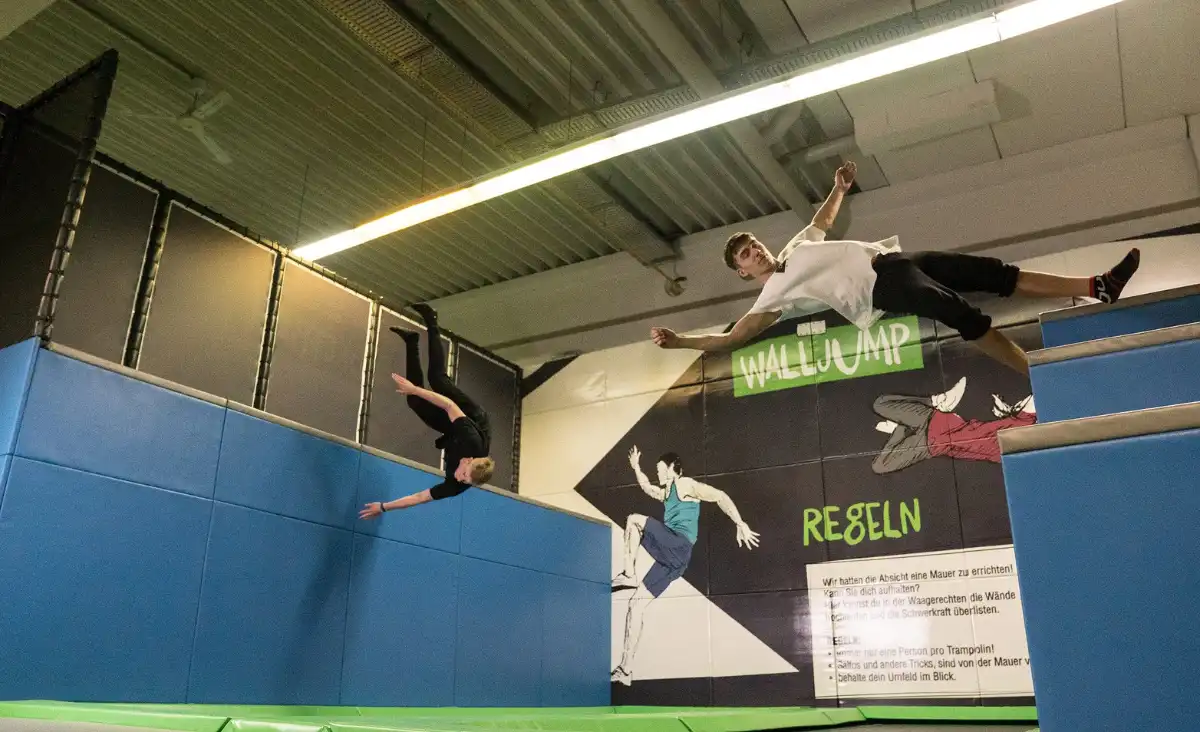 Zwei Personen springen auf Trampolinen in einer Indoor-Sporthalle und genießen die Aktivität.