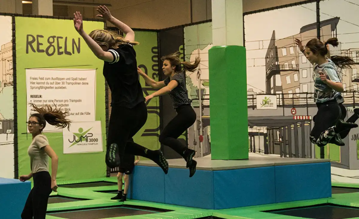 Eine Gruppe von Menschen springt fröhlich auf Trampolinen in einer Indoor-Anlage.