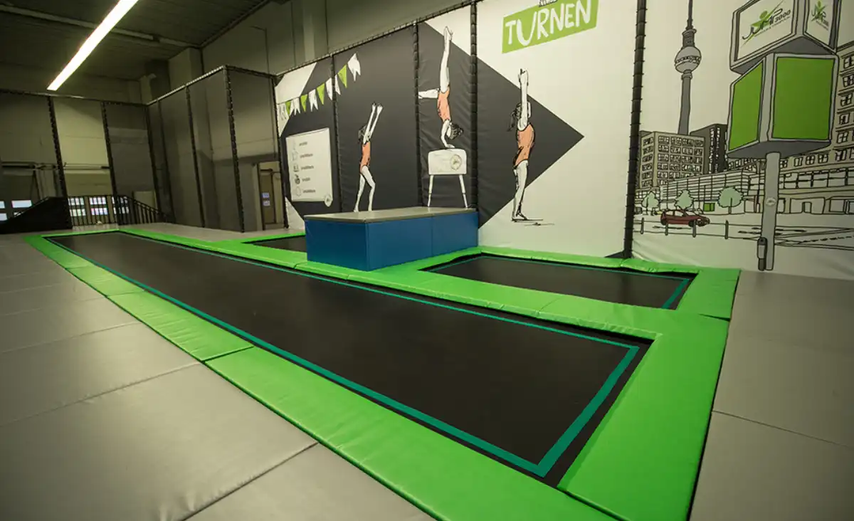 Ein Trampolin in einem großen Innenraum, umgeben von Wänden, bietet Platz für Sprünge und Aktivitäten.