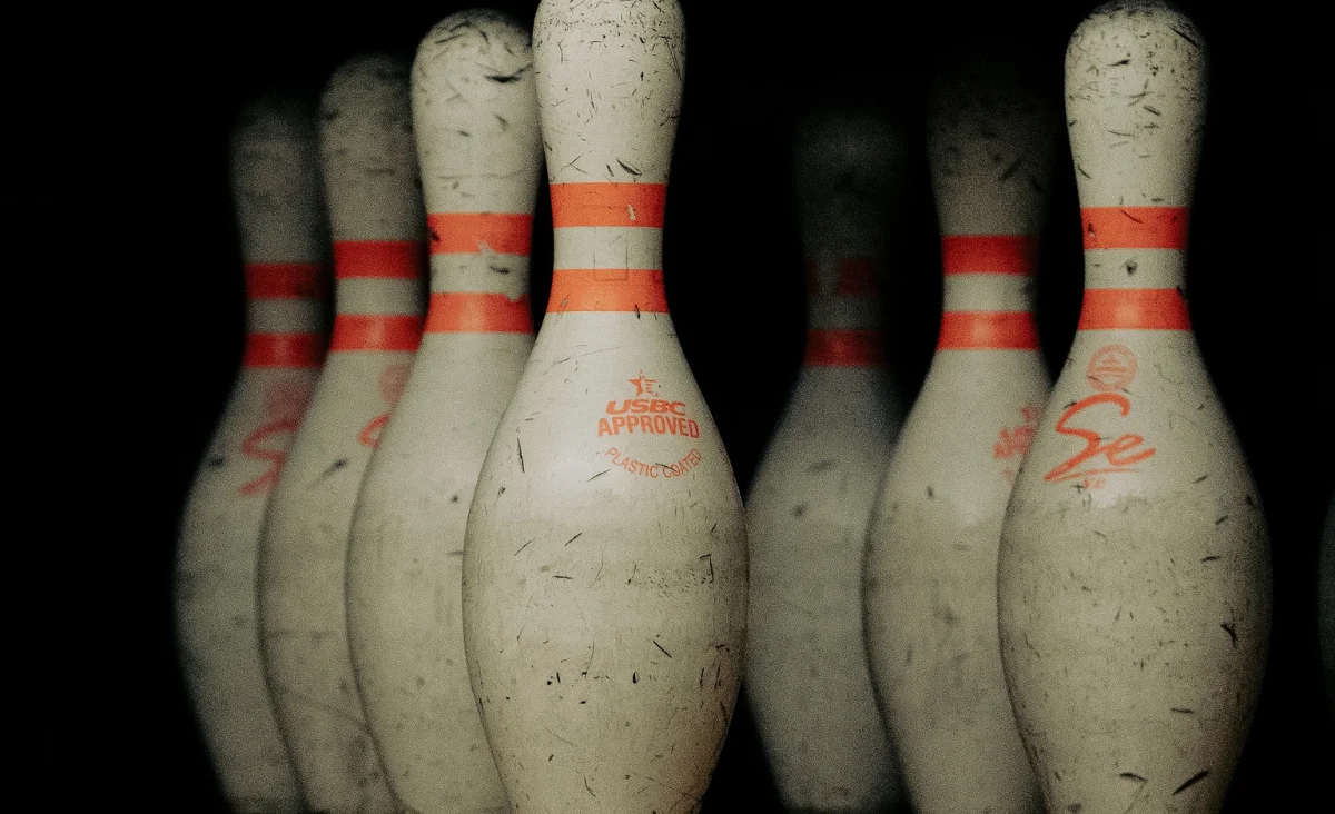 Eine Reihe von Bowlingkegeln mit orange-weißen Streifen steht auf der Bahn