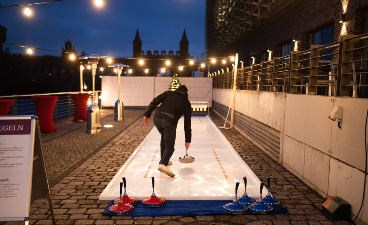Ein Mann spielt nachts Curling auf einer beleuchteten Curlingbahn.
