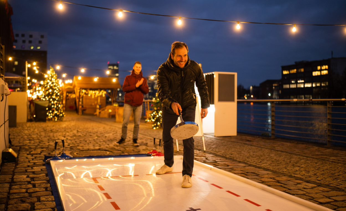 Ein Mann spielt Curling auf einer Eisbahn und zielt mit seinem Stein auf das Ziel.