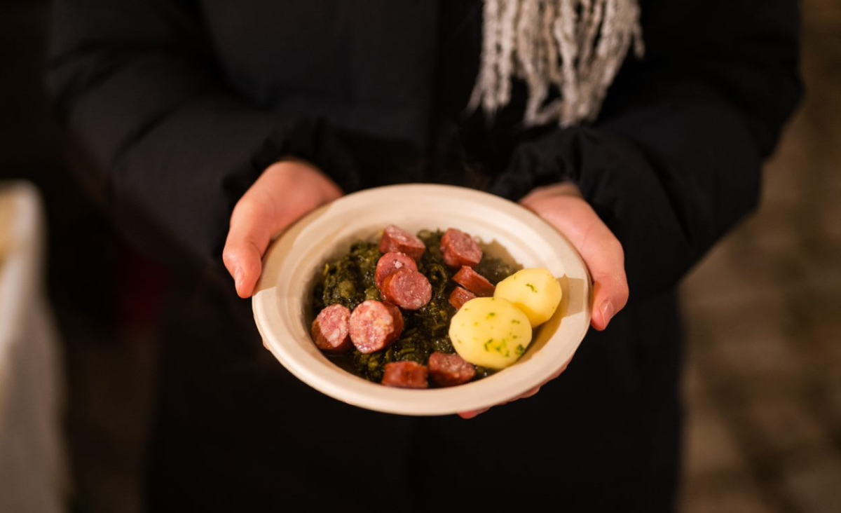Eine Person hält eine Schüssel mit Wurst und Kartoffeln in der Hand.