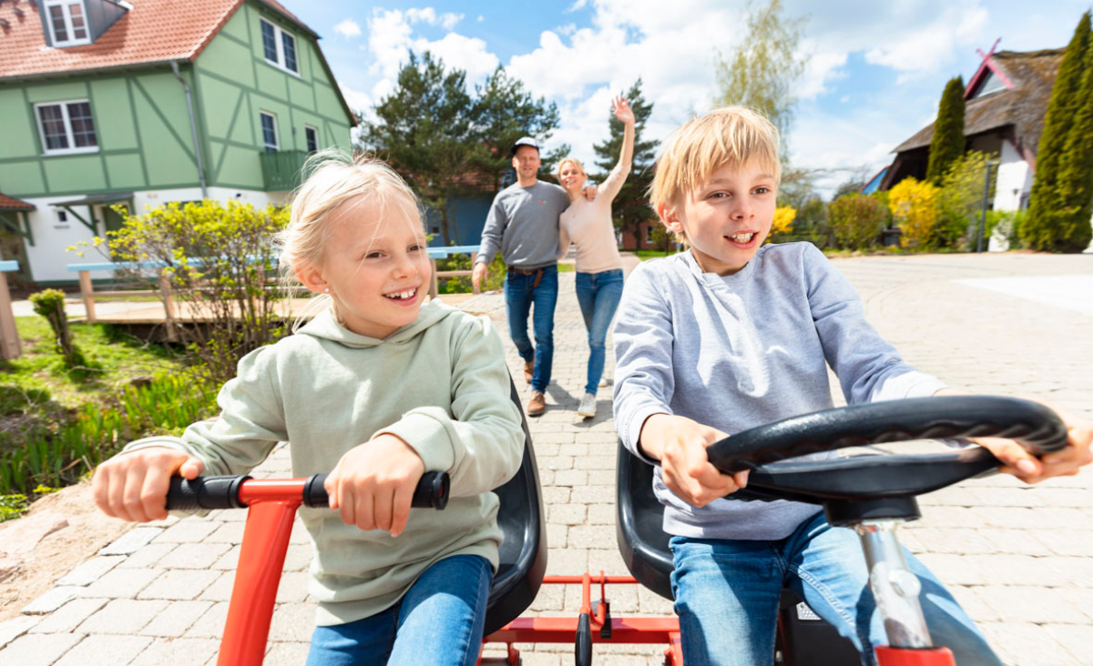 Zwei Kinder fahren auf einem Dreirad vor einem Haus und genießen ihren Tag voller Spaß und Abenteuer.