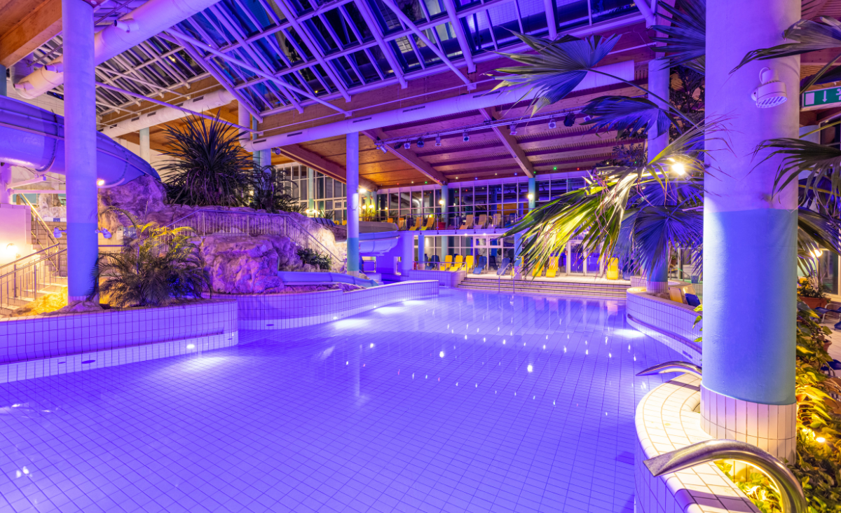 Ein großes Hallenbad mit einem weitläufigen Glasdach, das viel Tageslicht hereinlässt.