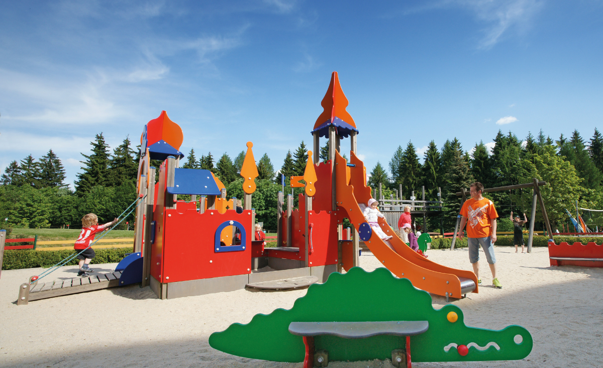 Ein sandfarbener Spielplatz mit verschiedenen Spielgeräten und einer einladenden Umgebung für Kinder.