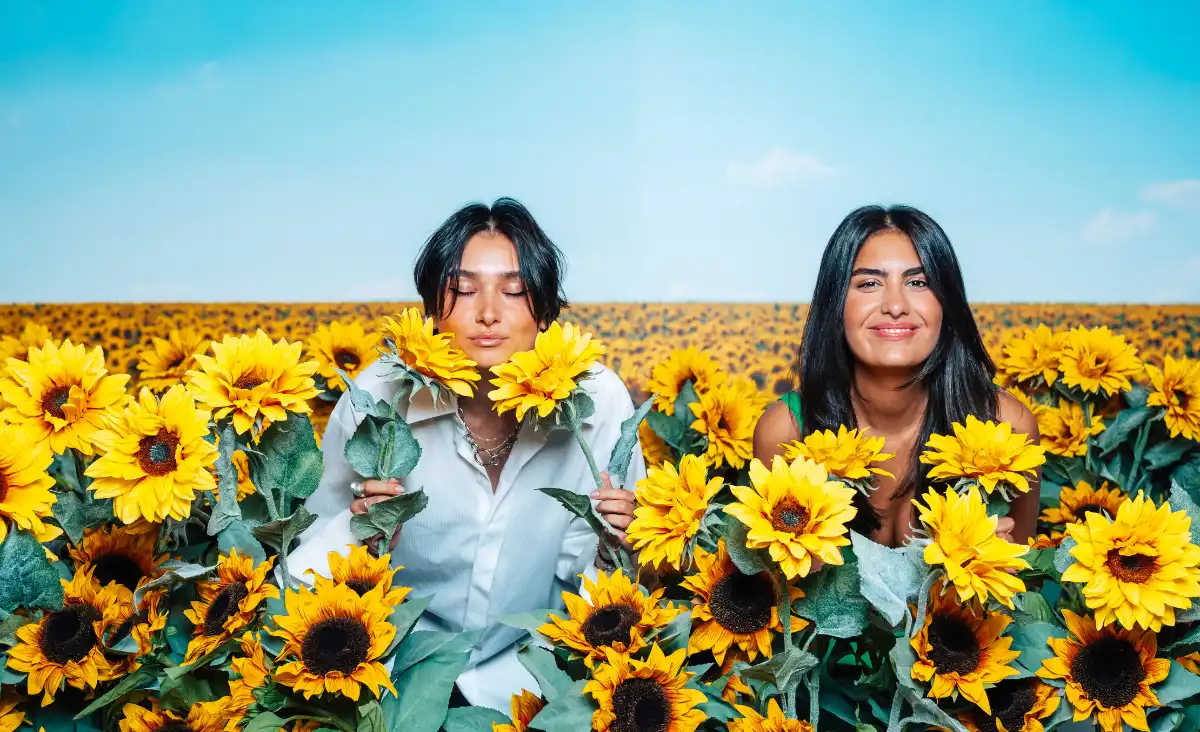 Zwei Frauen stehen in einem Sonnenblumenfeld und genießen die sonnige Atmosphäre und die blühenden Blumen um sie herum.