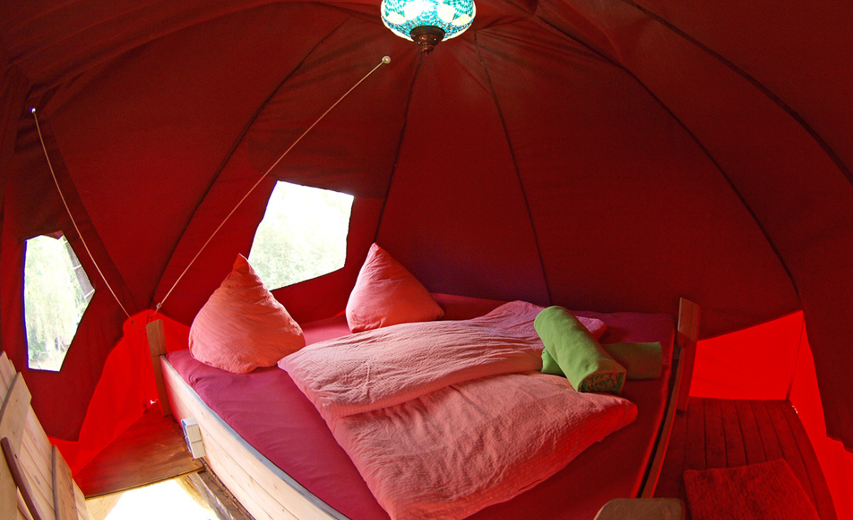 Ein gemütliches Bett in einem Zelt, umgeben von Natur und einem Hauch von Abenteuer.