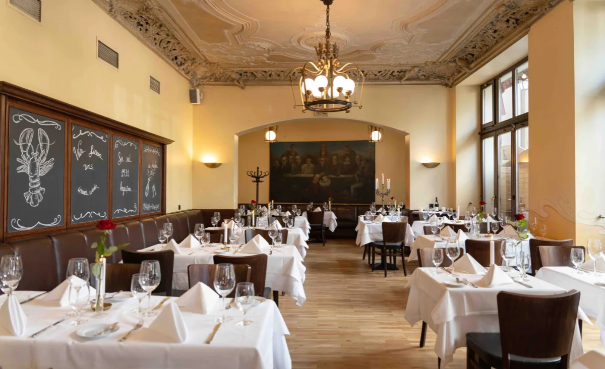 Innenansicht eines Restaurants mit mehreren Tischen und Stühlen, die für Gäste arrangiert sind.