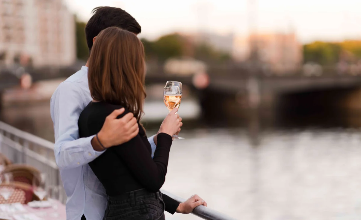 Ein Mann und eine Frau halten Champagnergläser auf einem Balkon mit Blick auf den Fluss.