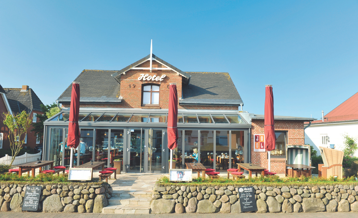 Der Eingang des Hotels Kiose auf Sylt mit einem markanten roten Dach, das die Aufmerksamkeit der Passanten auf sich zieht.