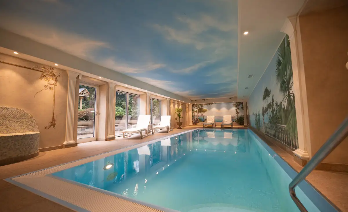 Weitläufiges Hallenbad, dessen Wand mit einem blauen Himmel gestaltet ist, ideal für Erholung und Spaß.