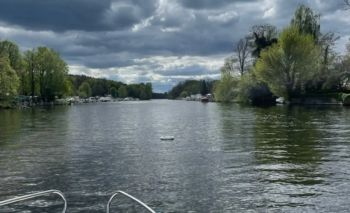 Ein Boot auf dem Fluss, umgeben von Bäumen und Wolken im Hintergrund. Eine friedliche Naturansicht.