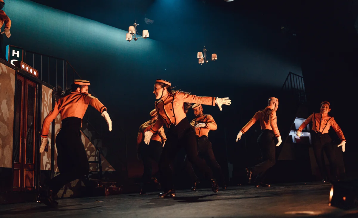 Tänzer in orangefarbenen Hemden und weißen Handschuhen führen auf der Bühne eine Darbietung von "The Tap Dance Sensation" auf.