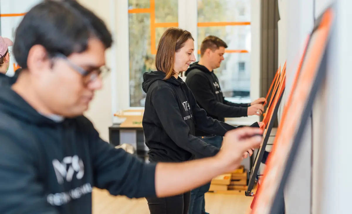 Gruppe von Personen in schwarzen Shirts und Hoodies, die an einem großen Kunstwerk arbeiten.