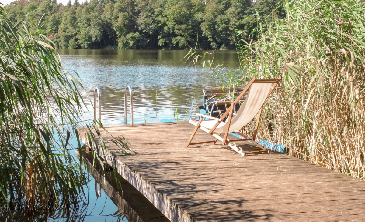 Ein hölzerner Steg mit einem Stuhl und einem Ruderboot, umgeben von ruhigem Wasser und natürlicher Umgebung.
