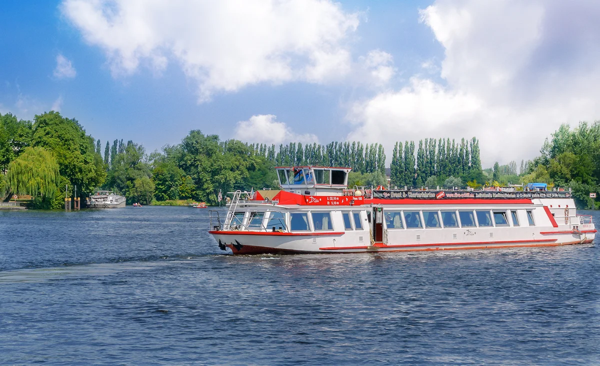 Ein Flussboot gleitet sanft über das Wasser, umgeben von einer malerischen Landschaft.