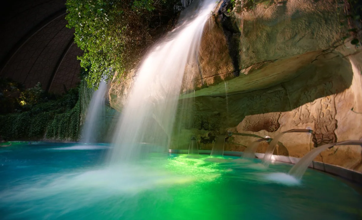 Ein Wasserfall, der in einen klaren Pool stürzt, umgeben von üppigem Grün und Felsen.
