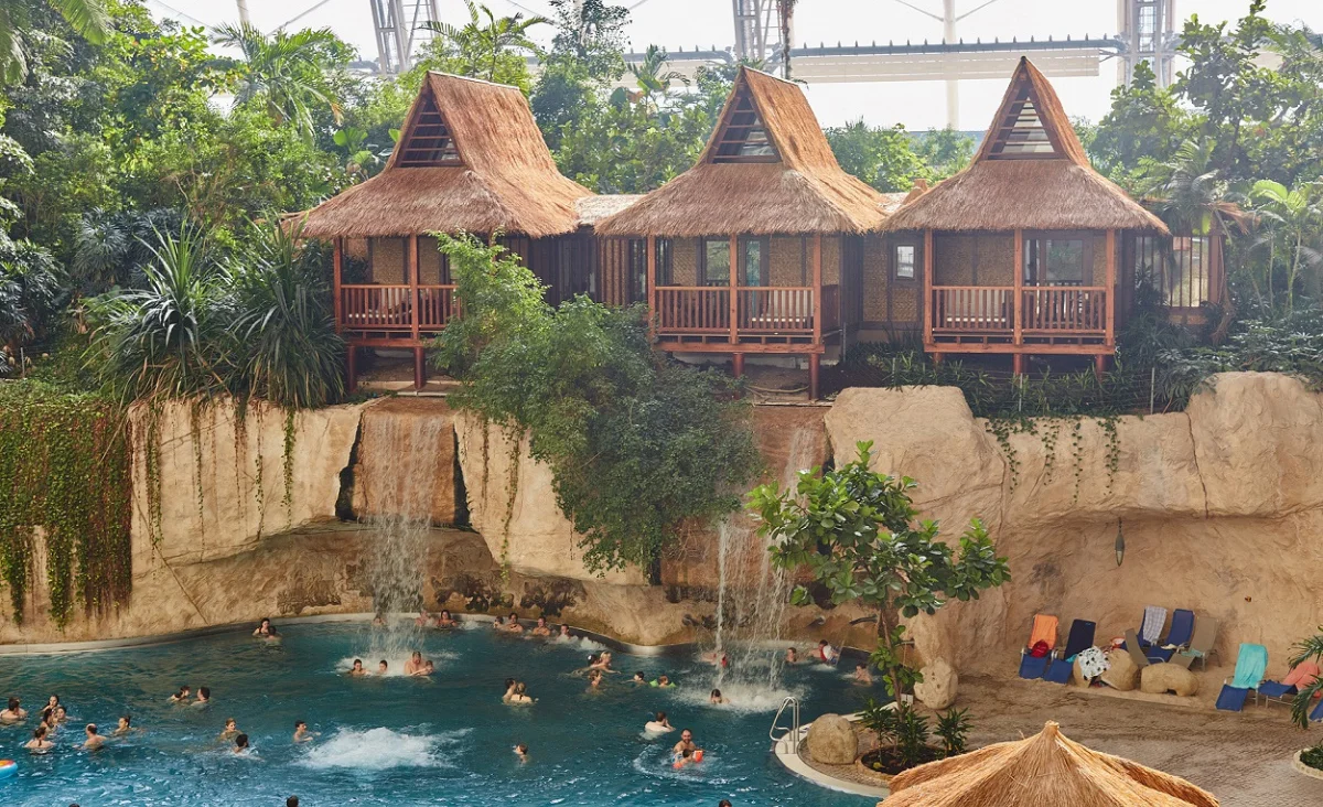 Ein großer Pool mit einem Wasserfall, der sanft ins Wasser plätschert, umgeben von üppiger Vegetation.