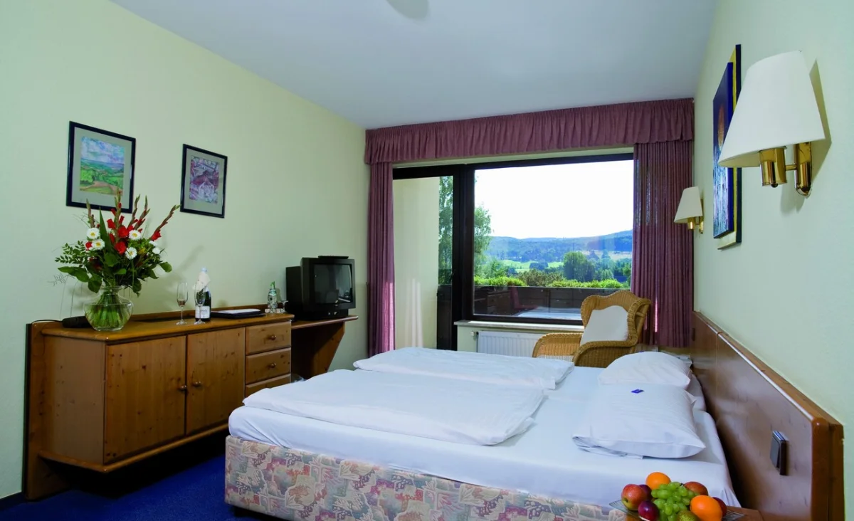 Ein Hotelzimmer mit einem Bett, einem Fernseher, einem Tisch und einem Fenster, das eine gemütliche Atmosphäre ausstrahlt.