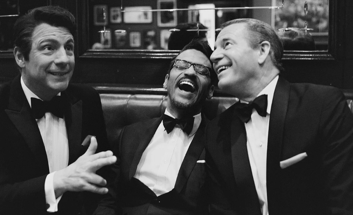 Drei elegant gekleidete Männer in Smokings lachen herzlich und teilen einen fröhlichen Augenblick.