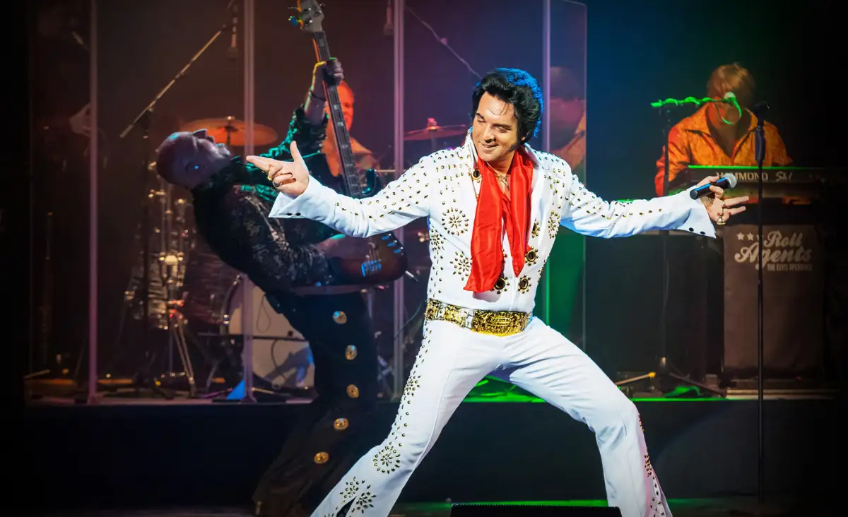 Ein Sänger der Elvis Presley imitiert live auf der Bühne, umgeben von anderen Musikern, in der Show "THE MUSICAL STORY OF ELVIS".