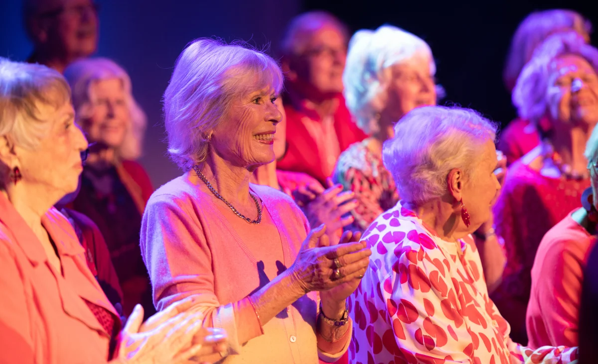 Eine Seniorin klatscht begeistert mit einer Gruppe von Menschen in der Menge beim Auftritt des Chors "Heaven can wait".