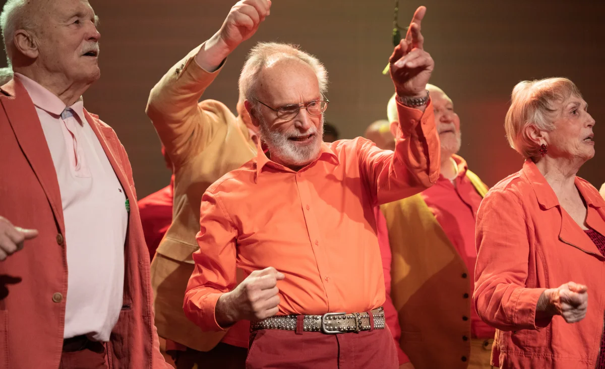 Eine Gruppe von Senioren in orangefarbener Kleidung, die stolz für den Chor "Heaven can wait" posiert.