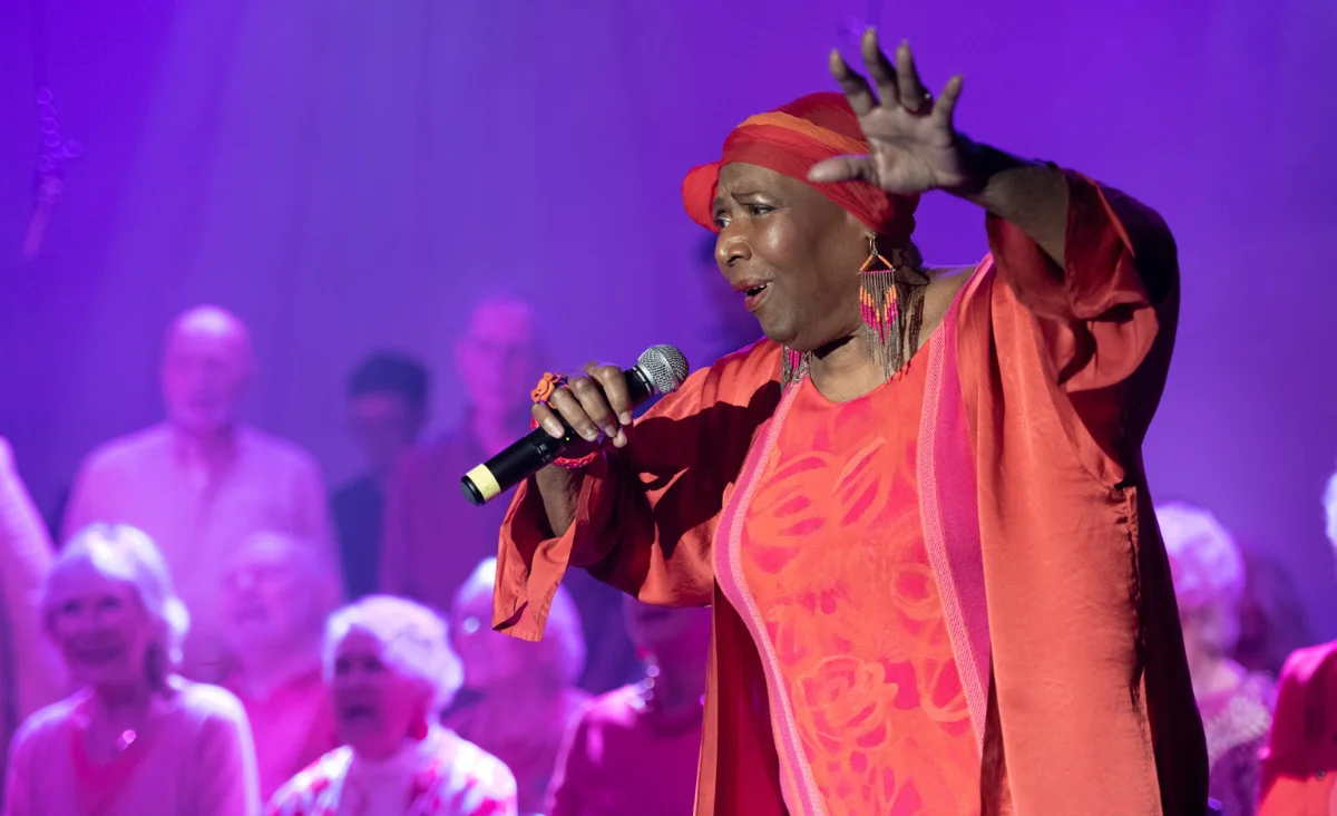 Eine Frau in rotem Kleid steht am Mikrofon und singt für den Chor von "Heaven can wait".
