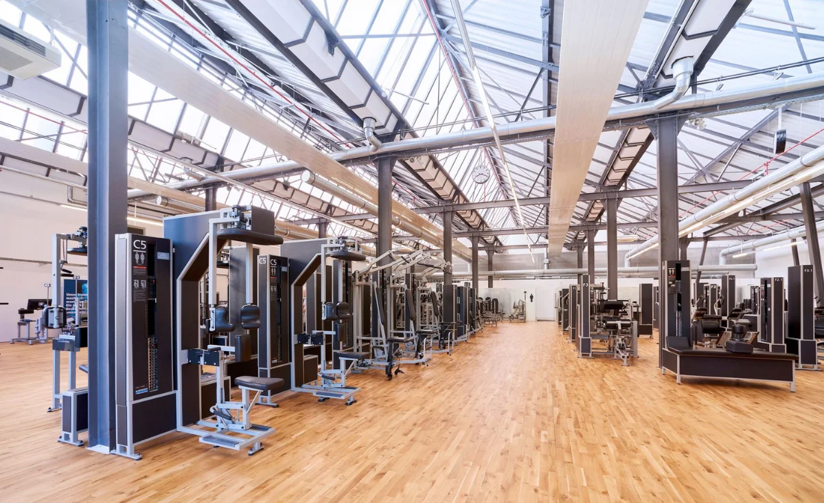 Innenraum eines Kieser Training Studios Berlin mit mehreren Krafttrainingsgeräten auf Holzboden und großen Fenstern