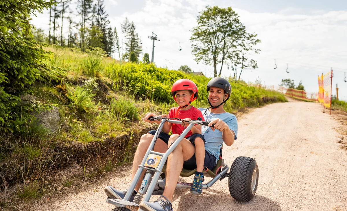 Ein Mann und ein Kind fahren gemeinsam auf einem Quad in Wurzelrudis Erlebniswelt.