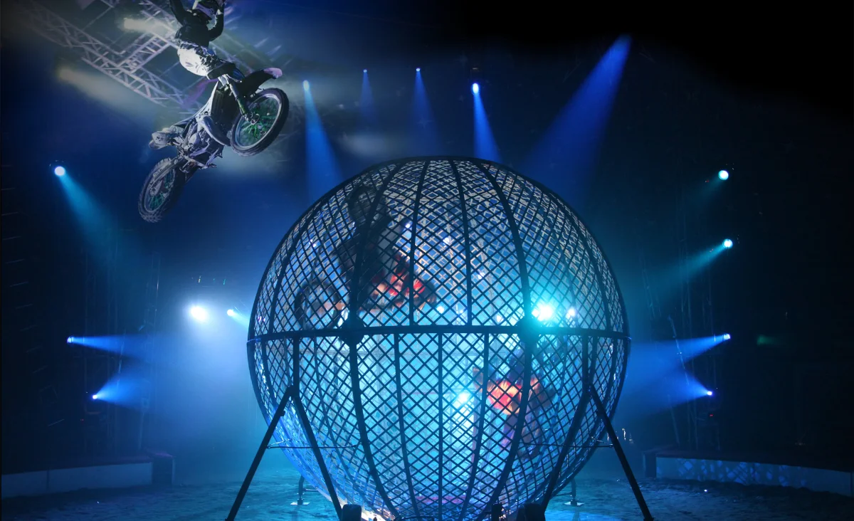 Zirkus des Horrors Memento Mori in Berlin: Ein Mann fährt auf einem Motorrad in einem beleuchteten Käfig.