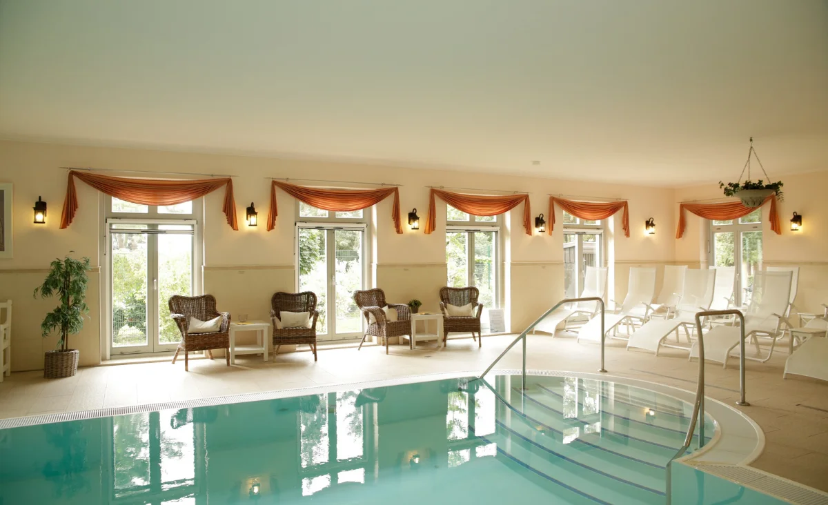 Ein großes Hallenbad mit einer Leiter und Liegen am Beckenrand.
