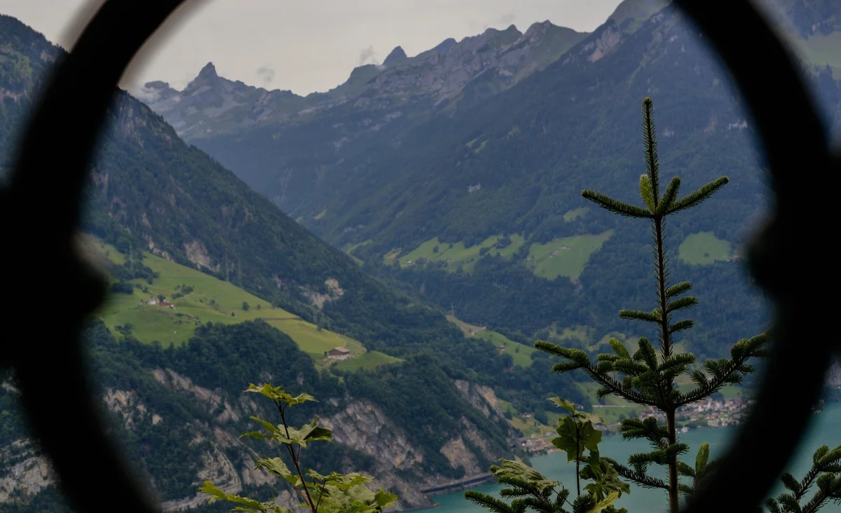 Rundes Fenster mit Aussicht auf den Vierwaldstättersee und die umliegenden Berge.