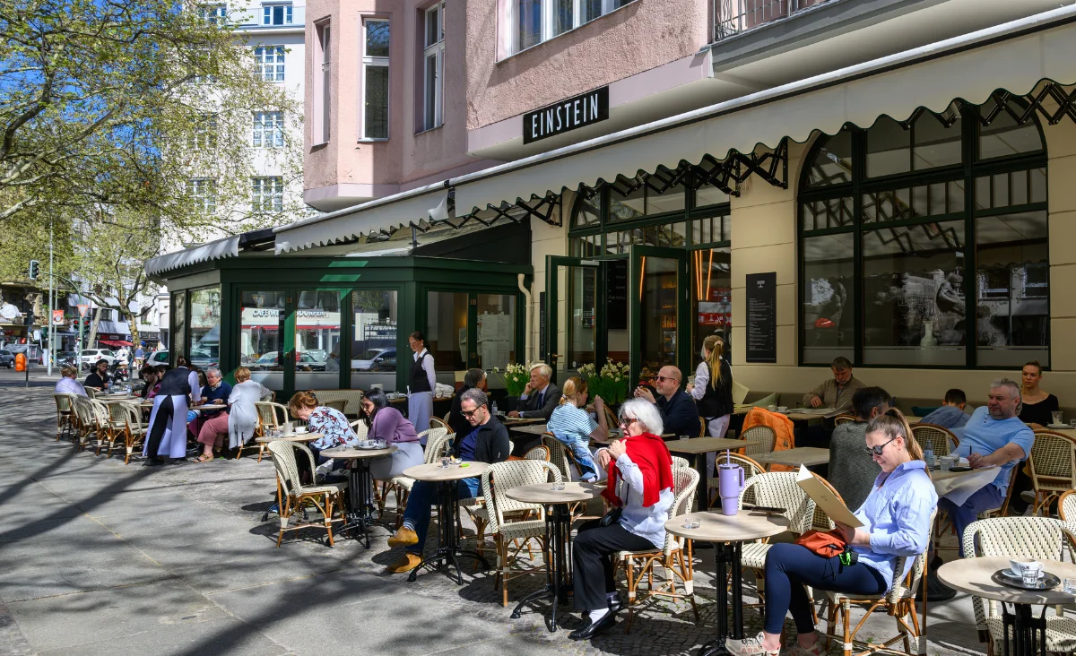 Gäste genießen die Sonne an Tischen vor dem Café Das Einstein-Mommseneck.