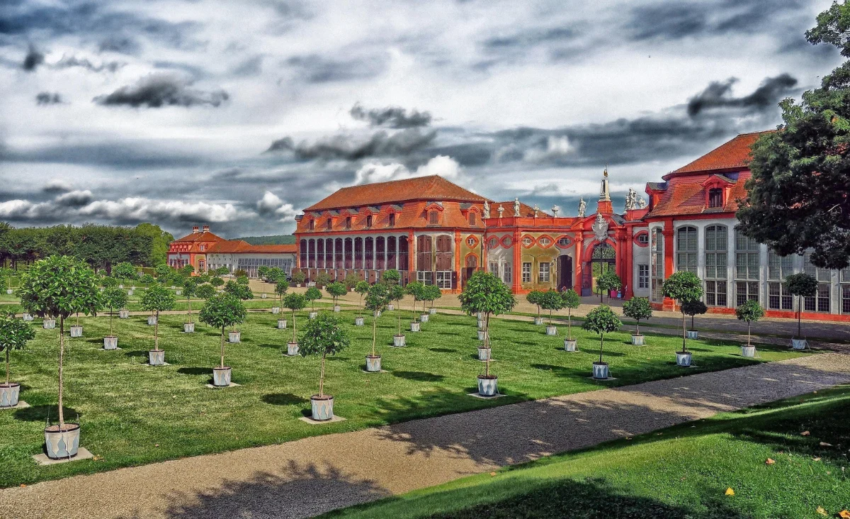 Großes rotes Gebäude vor einer Wiese mit Bäumen.