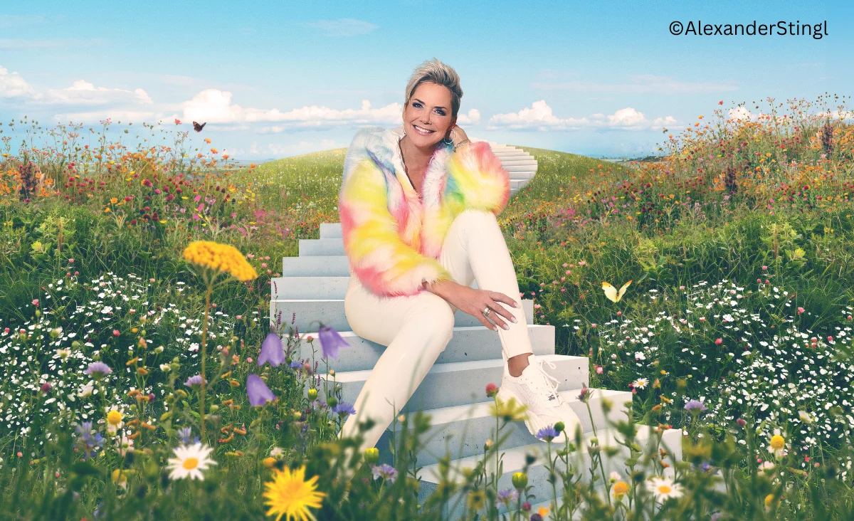 Auf einer weißen Treppe sitzt Inka Bause umgeben von bunten Blumen in einem Feld.