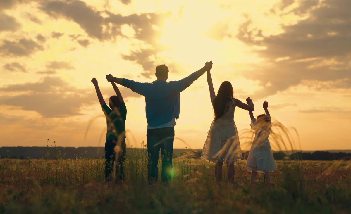 Eine Familie mit erhobenen Händen steht in einem weiten Feld und genießt den Moment.