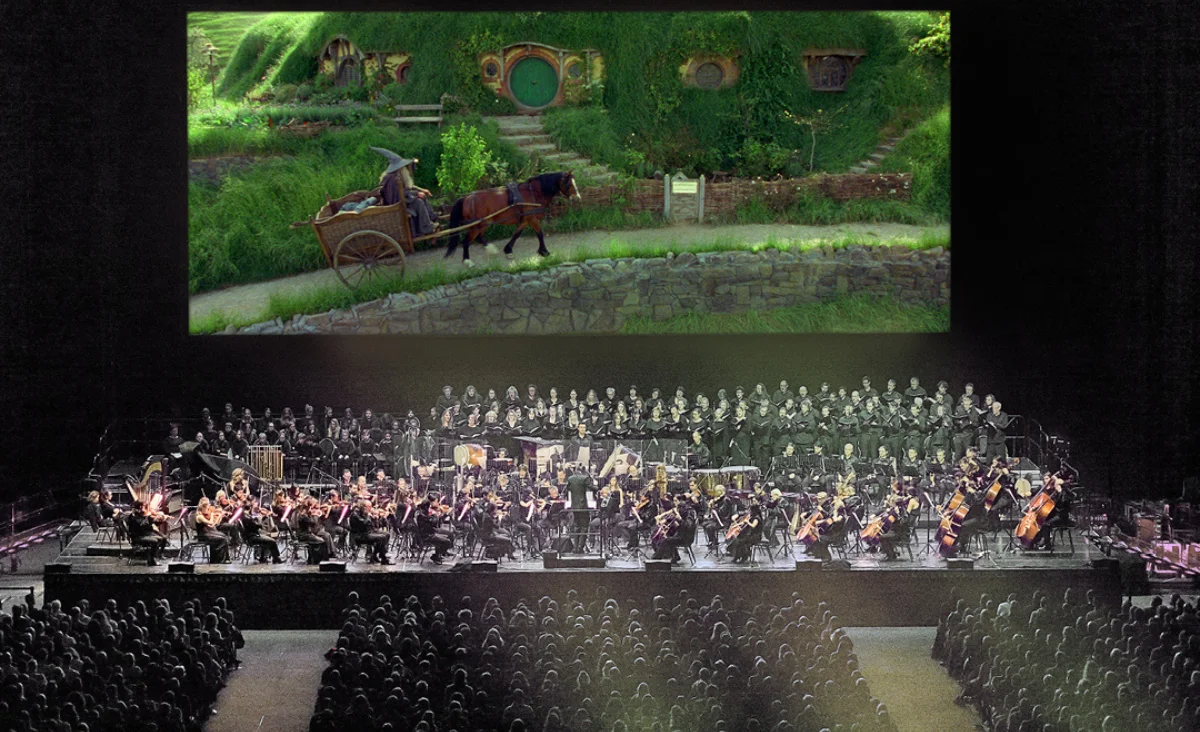 Eine große Aufführung eines Orchesters vor einem grünen Hintergrund auf einem großen Bildschirm.