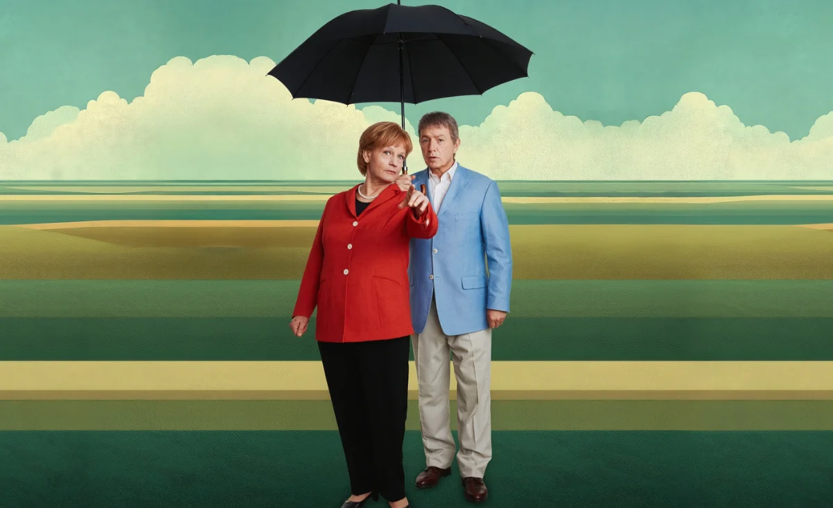 Die Schauspieler der Aufführung von "Miss Merkel" gehen unter einem Regenschirm.