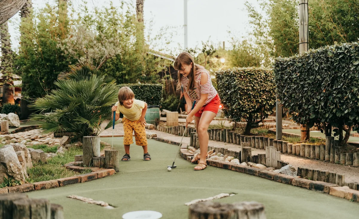 Zwei Kinder spielen begeistert Mini-Golf auf einem bunten Miniatur-Golfplatz während ihres Familienurlaubs an der Ostsee.