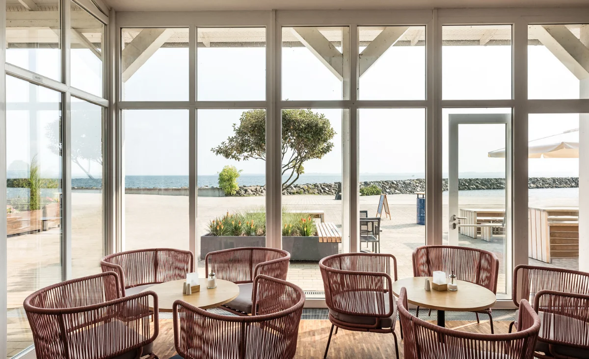 Ein Restaurant mit großen Fenstern, das einen Blick auf den Ozean bietet, ideal für einen Familienurlaub an der Ostsee.