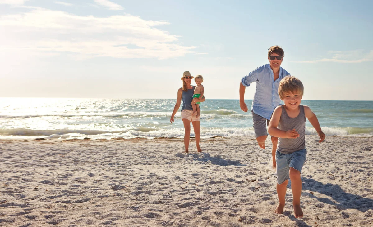 Ein Mann und eine Frau laufen mit einem Kind am Strand, fröhlich während ihres Familienurlaubs an der Ostsee.