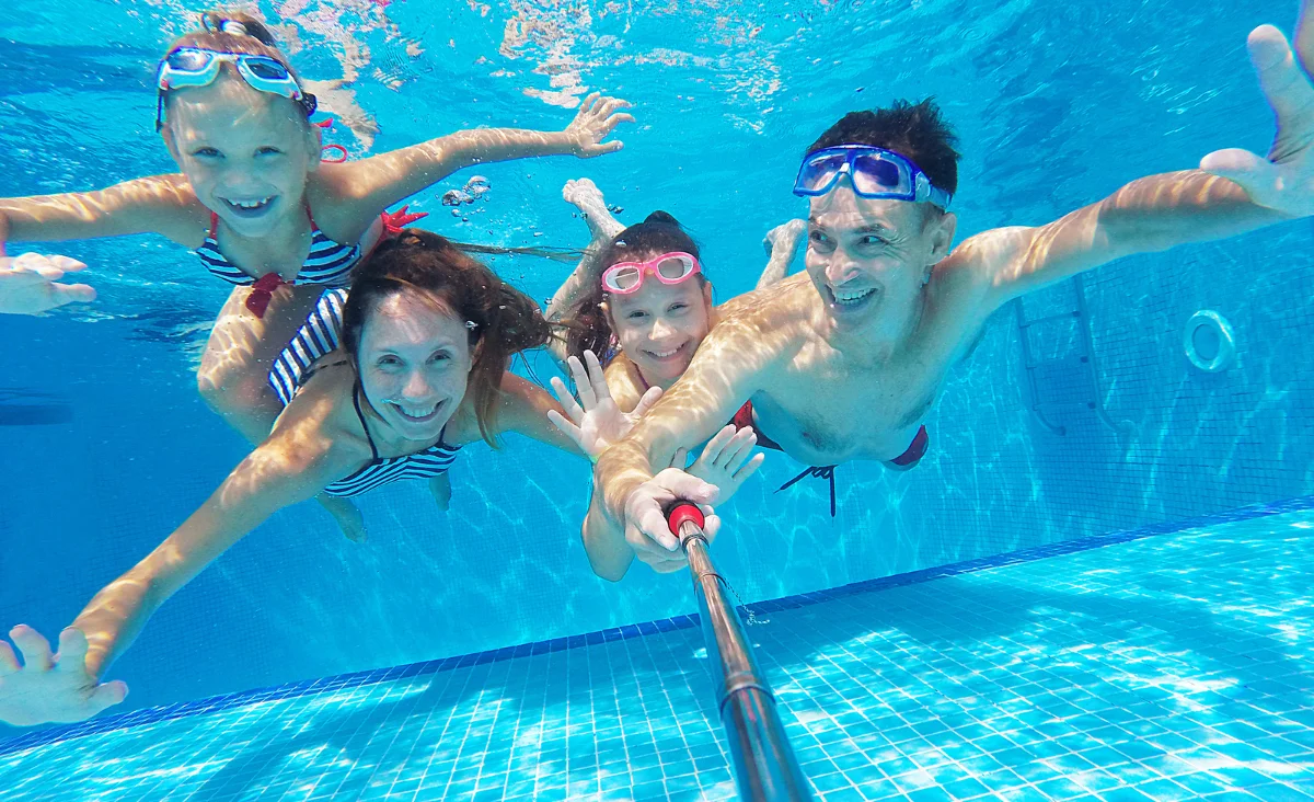 Eine Familie macht mit einem Selfie-Stick ein Foto beim Schwimmen im Pool während ihres Urlaubs an der Ostsee.