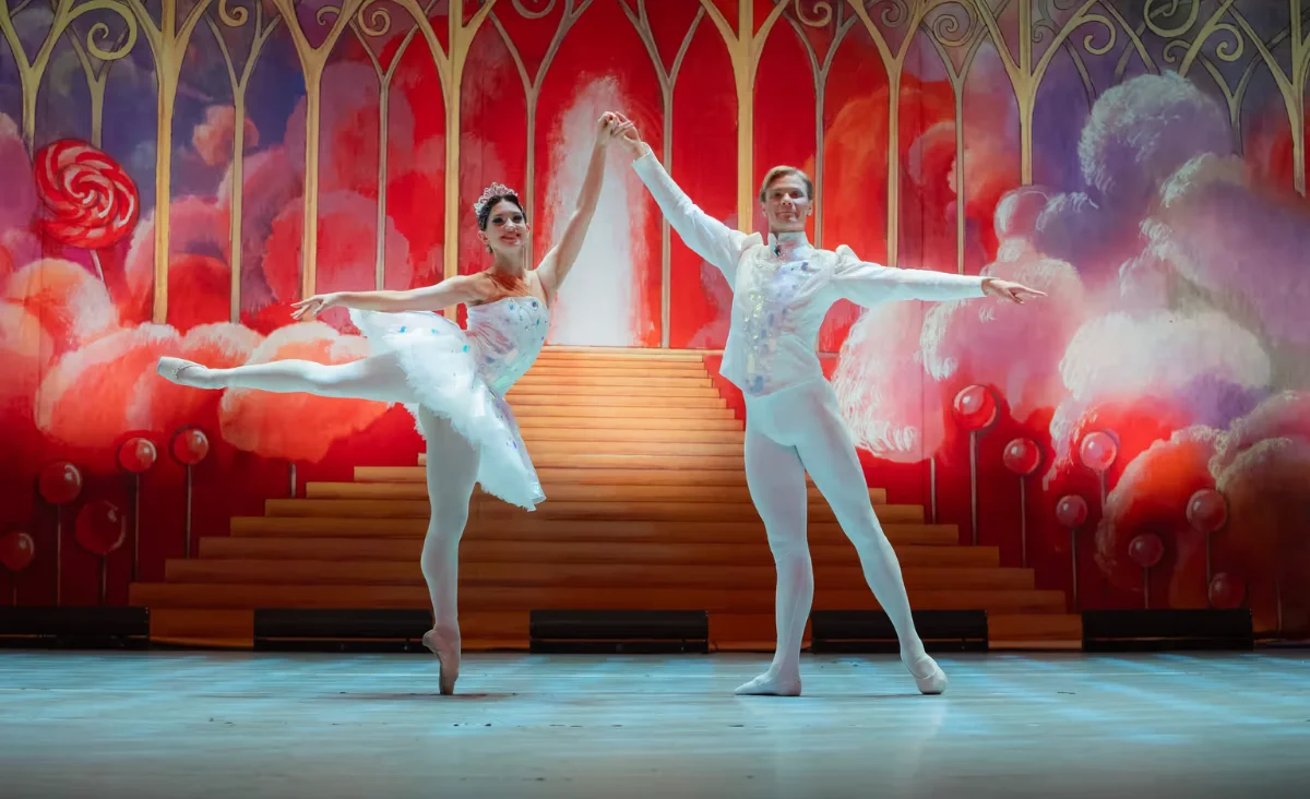Zwei Ballett-Tänzer in weißen Tutus tanzen auf der Bühne, im Hintergrund eine große Kulisse aus "Der Nussknacker".