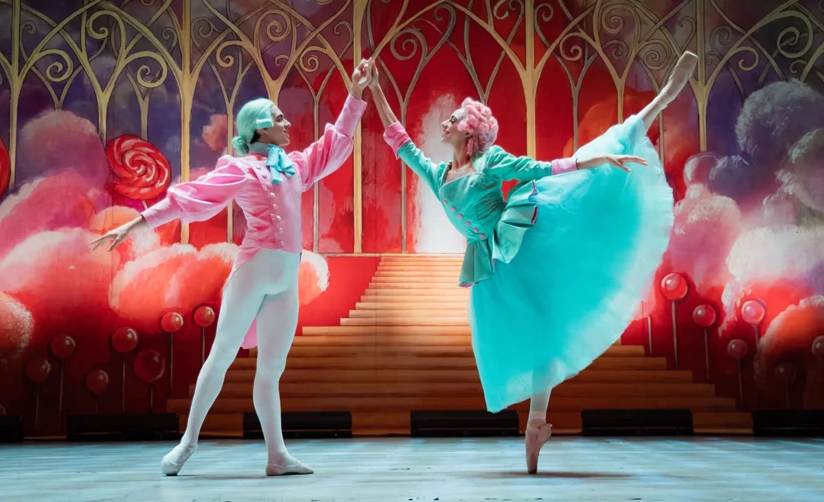 Auf der Bühne führen zwei Ballett-Tänzer in pink und blauem Kostüm eine Darbietung aus "Der Nussknacker" auf.