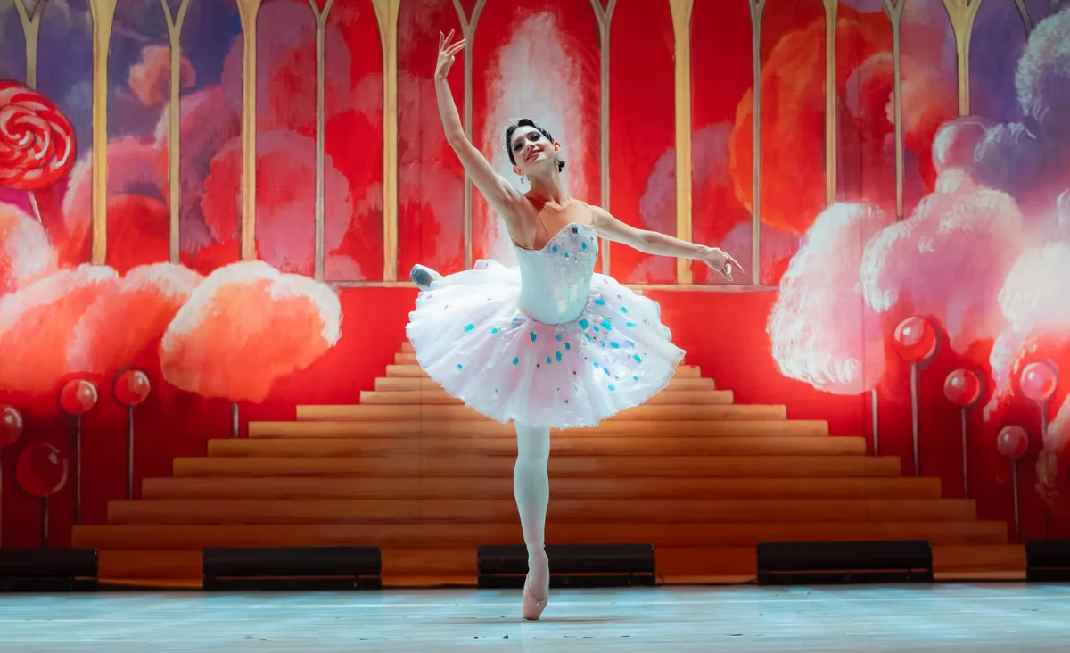 Auf der Bühne steht eine Ballerina in weißen Tutu, umgeben von einer beeindruckenden Kulisse des Balletts "Der Nussknacker".