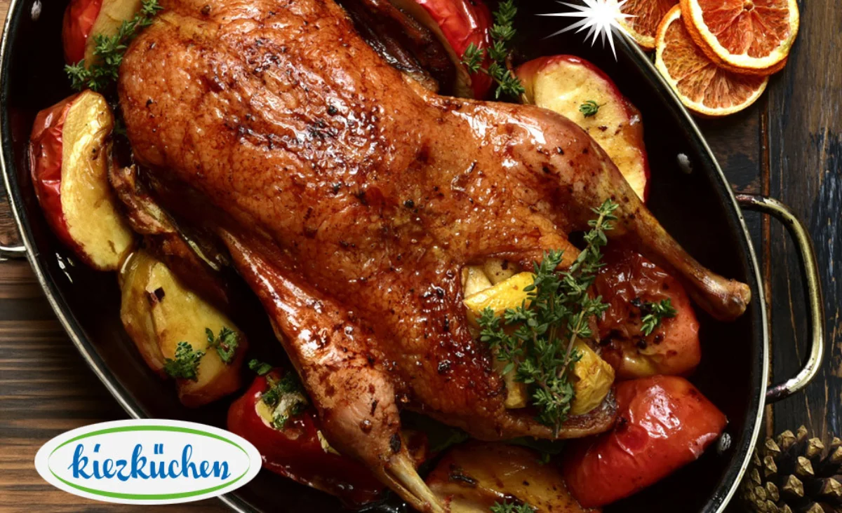 Eine gebratene Gans mit Gemüse und Orangen auf einem Holztisch, präsentiert von der Kiezküchen.