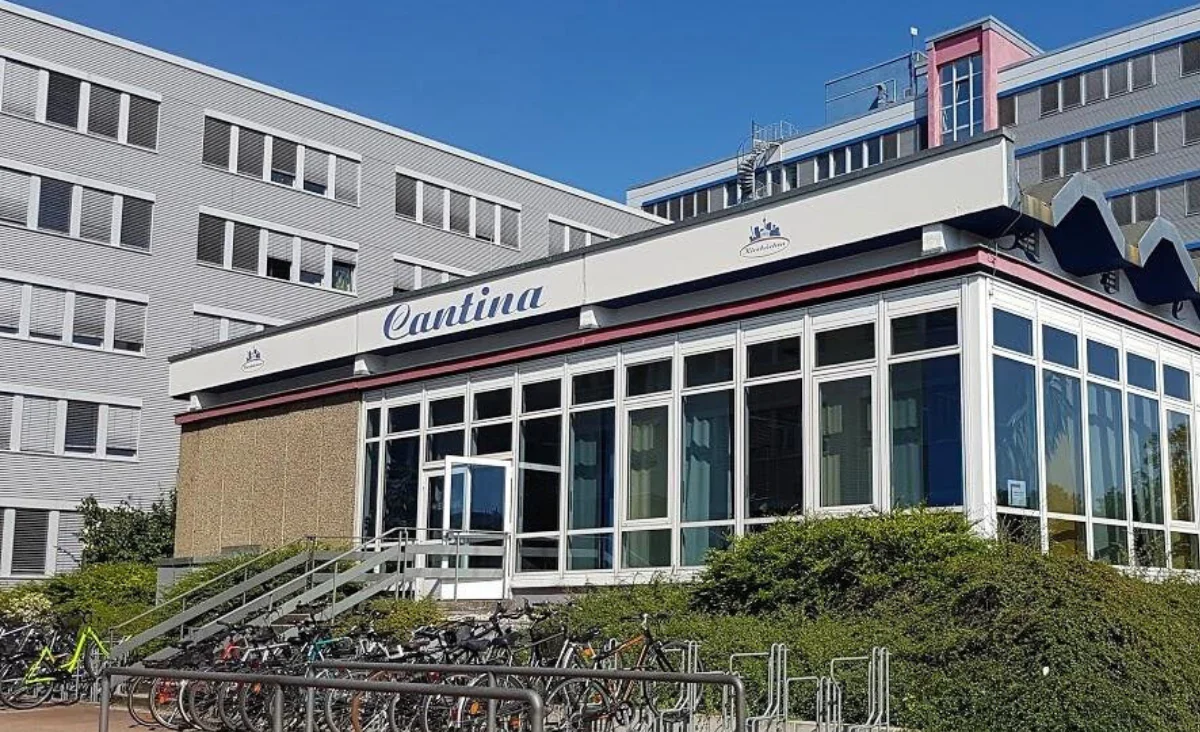 Die Fassade der Cantina zeigt große Glasfenster und einen Fahrradständer im Vordergrund.