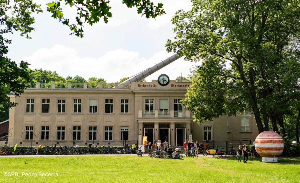 Großes Gebäude mit Uhrturm und einem großen Baum, Archenhold-Sternwarte, Planetarium Berlin.